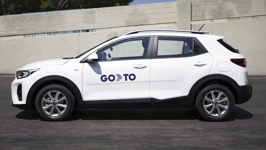 A white SUV with GoTo branding parked on a paved road, featuring the "GoTo" logo on the side. The vehicle is part of the GoTo car-sharing service, with a clean and modern design.