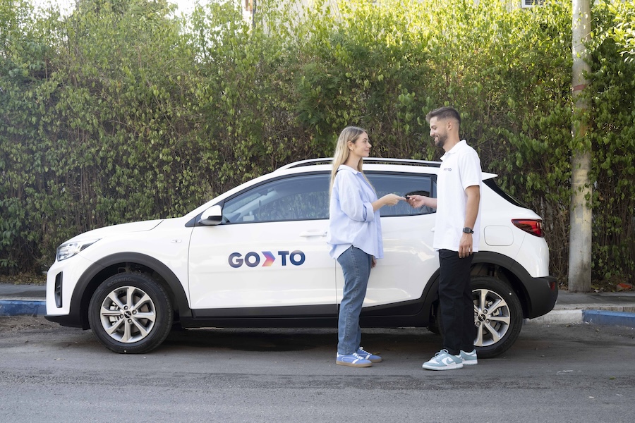 A business professional handing car keys to a customer next to a GoTo-branded car, showcasing a seamless car rental for business service.